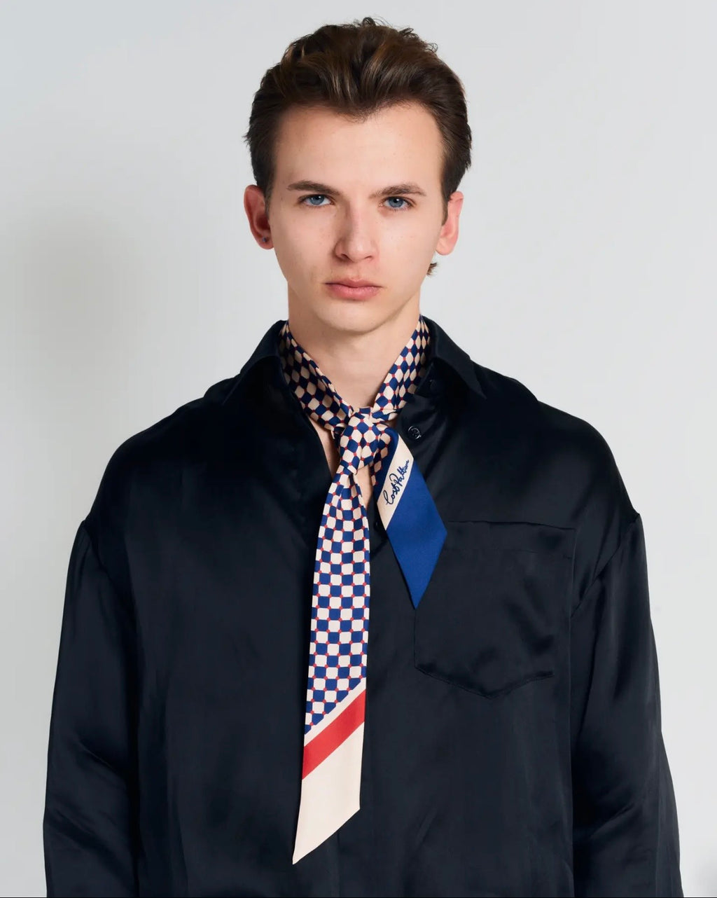 Man wearing a patterned scarf with visible branding on a plain background