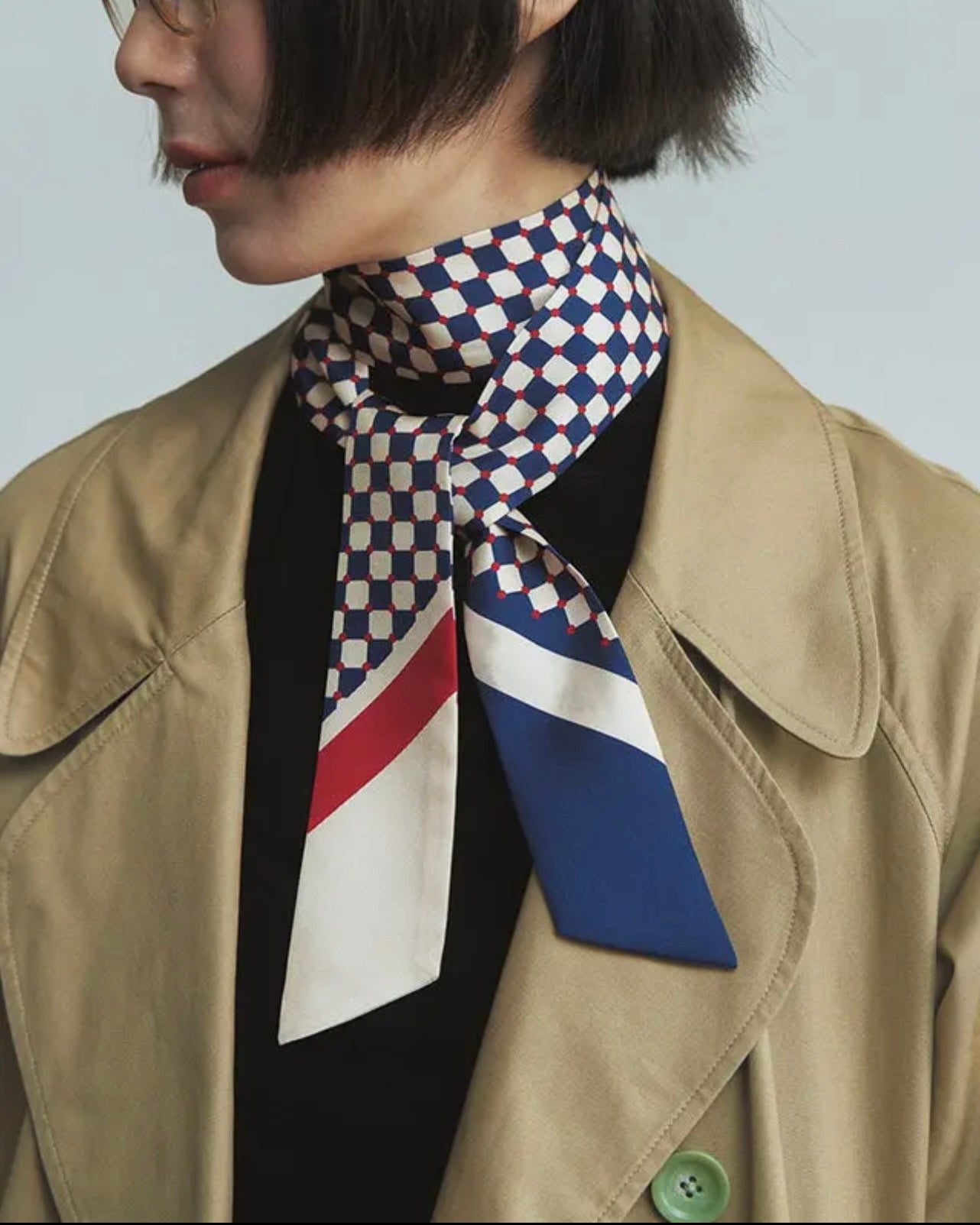 Person wearing a patterned scarf with a checkered design, standing against a plain background.