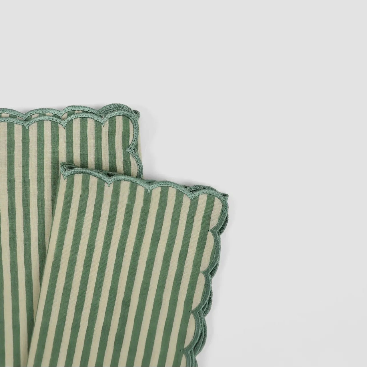 Pair of green and white stripe napkins with scalloped edge on a white background.