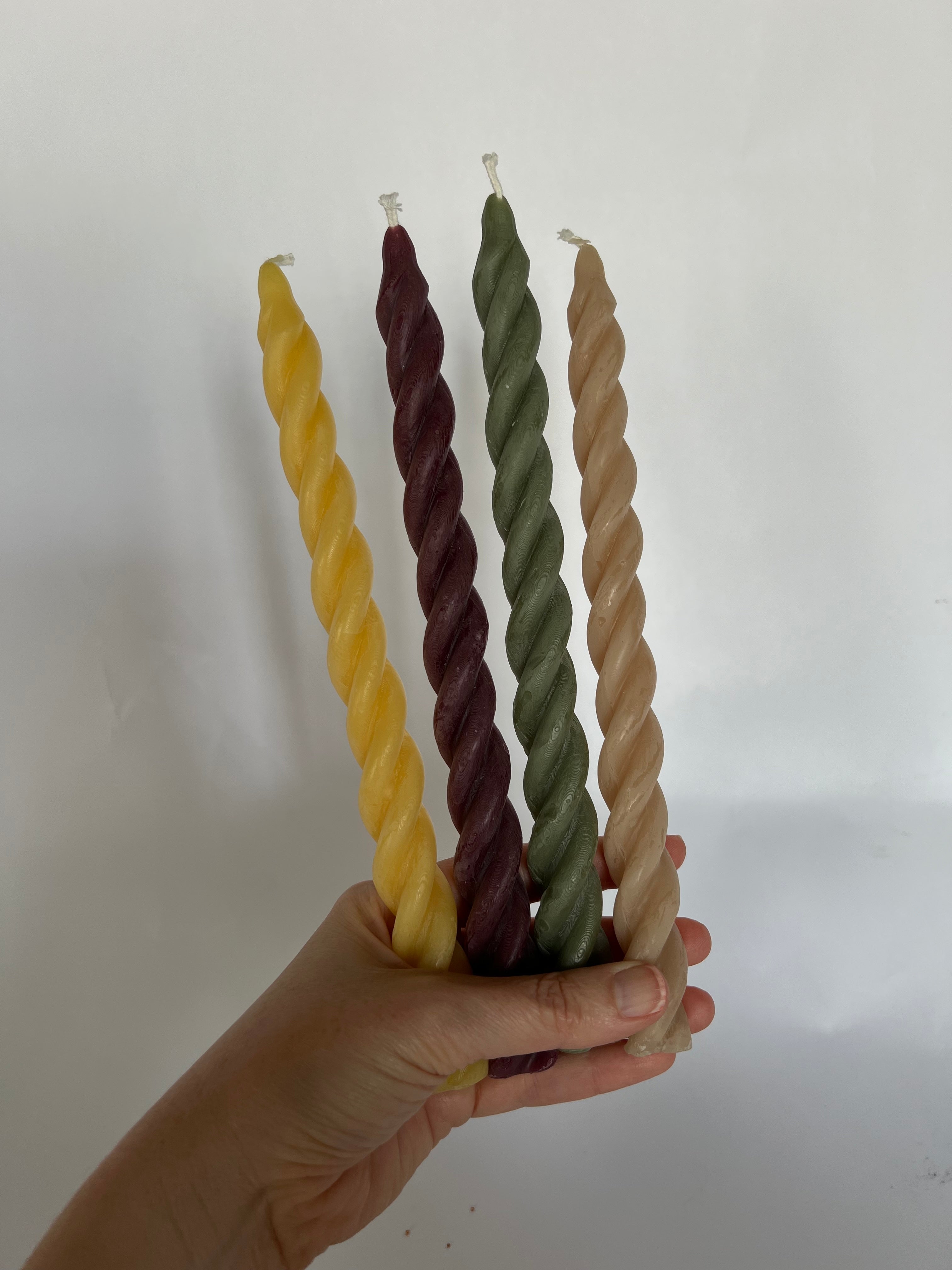 Hand holding four twisted candles in yellow, purple, green, and beige against a white background