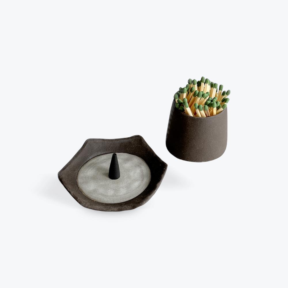 Two ceramic items on a white background, one is a dish with incense cone and the other with matches.