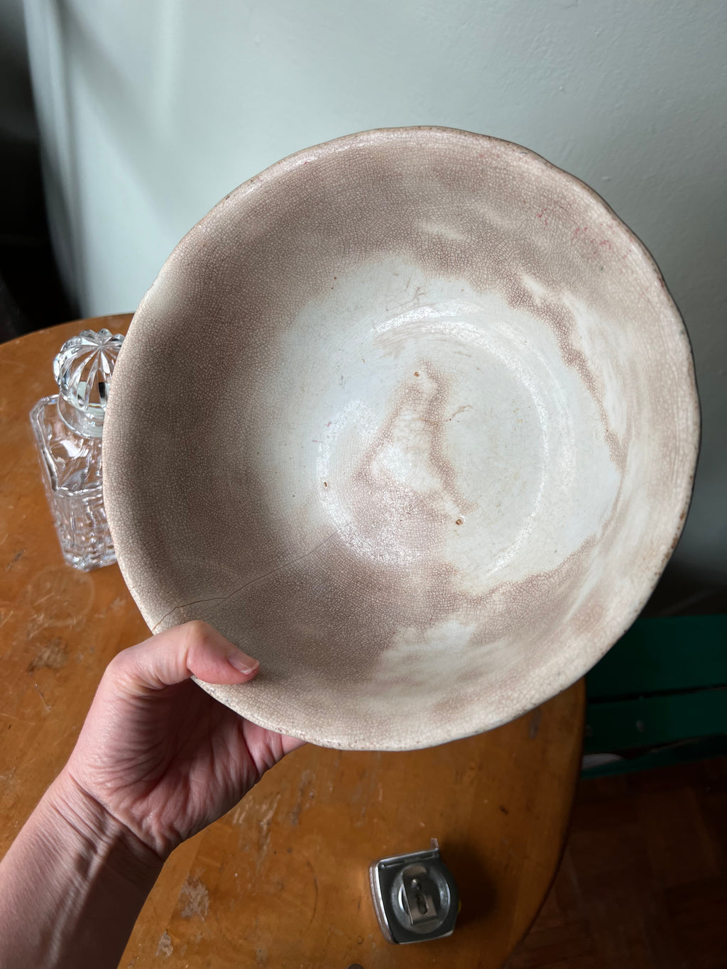 Hand holding a ceramic bowl on a wooden surface with a glass container in the background.