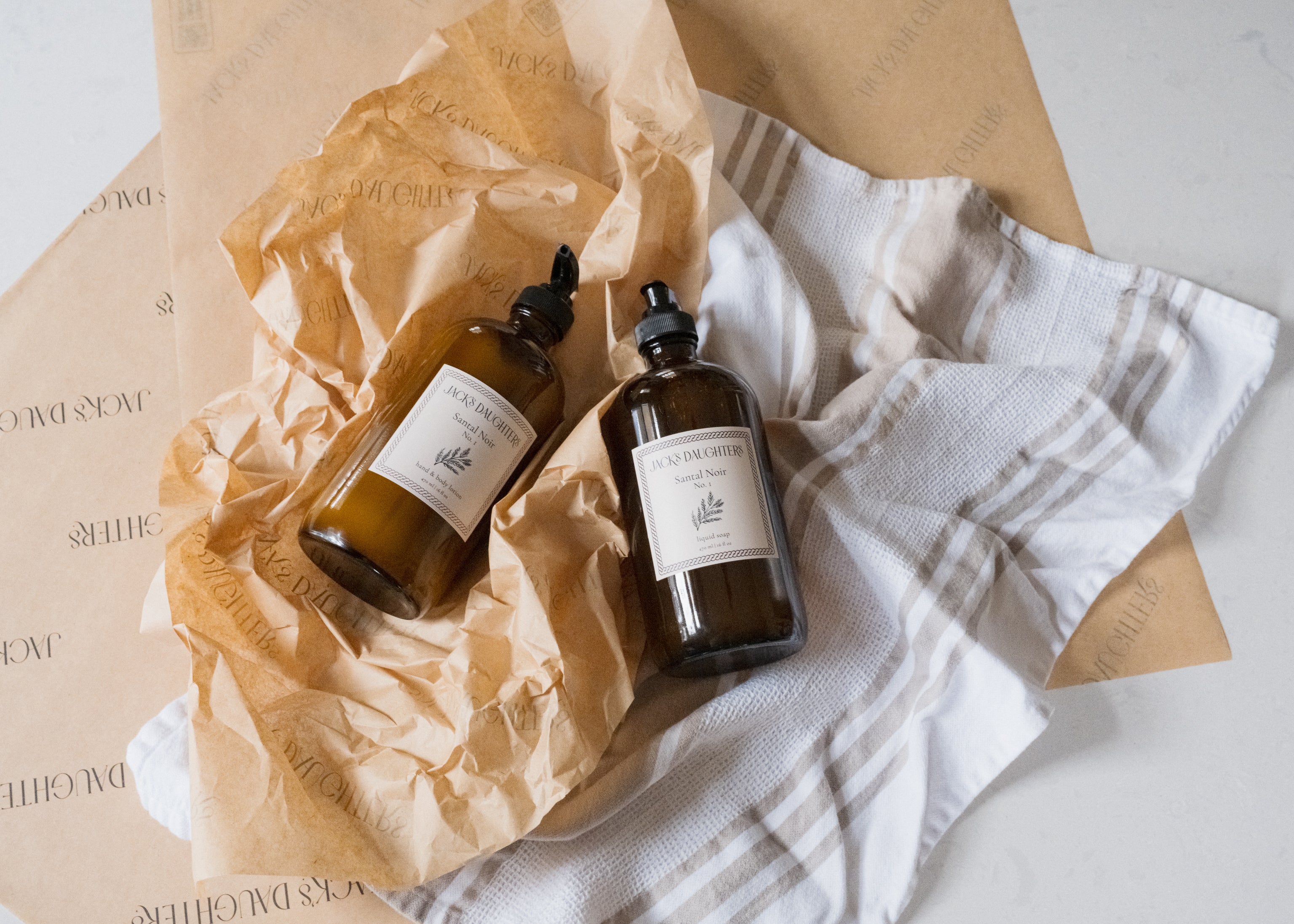 Two amber glass bottles of soap and lotion on a textured surface with a white cloth.