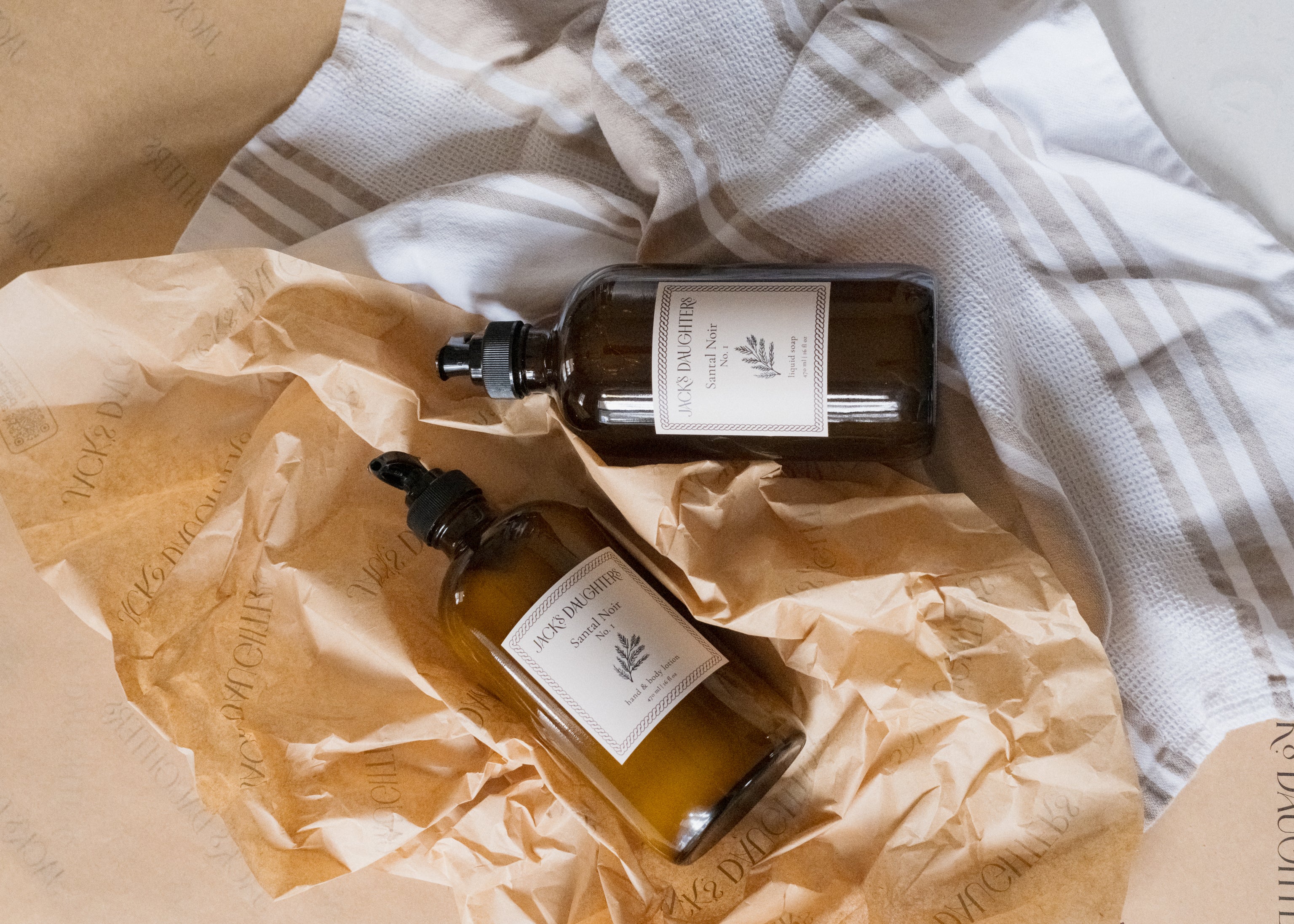 Two amber glass bottles of soap and lotion on a textured surface with a white cloth.