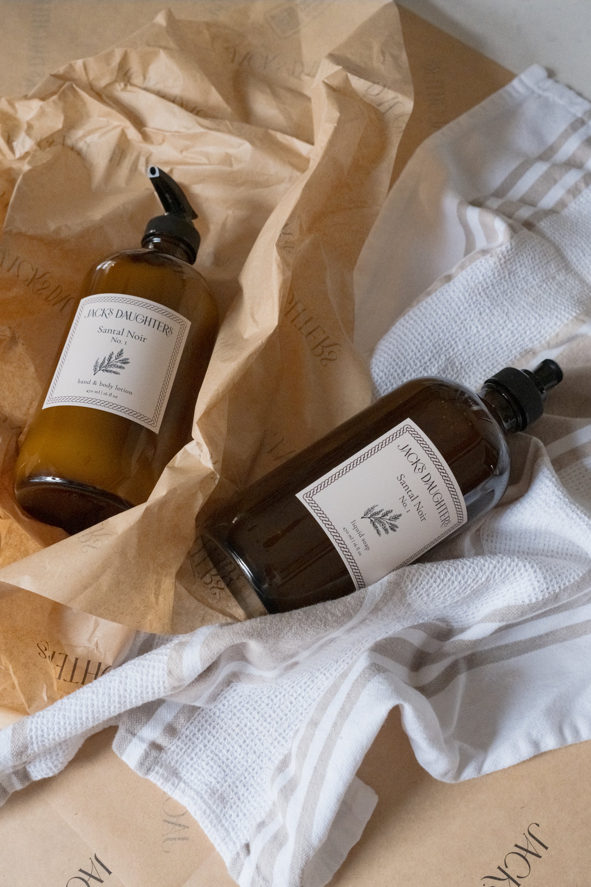 Two amber glass bottles of soap and lotion on a textured surface with a white cloth.