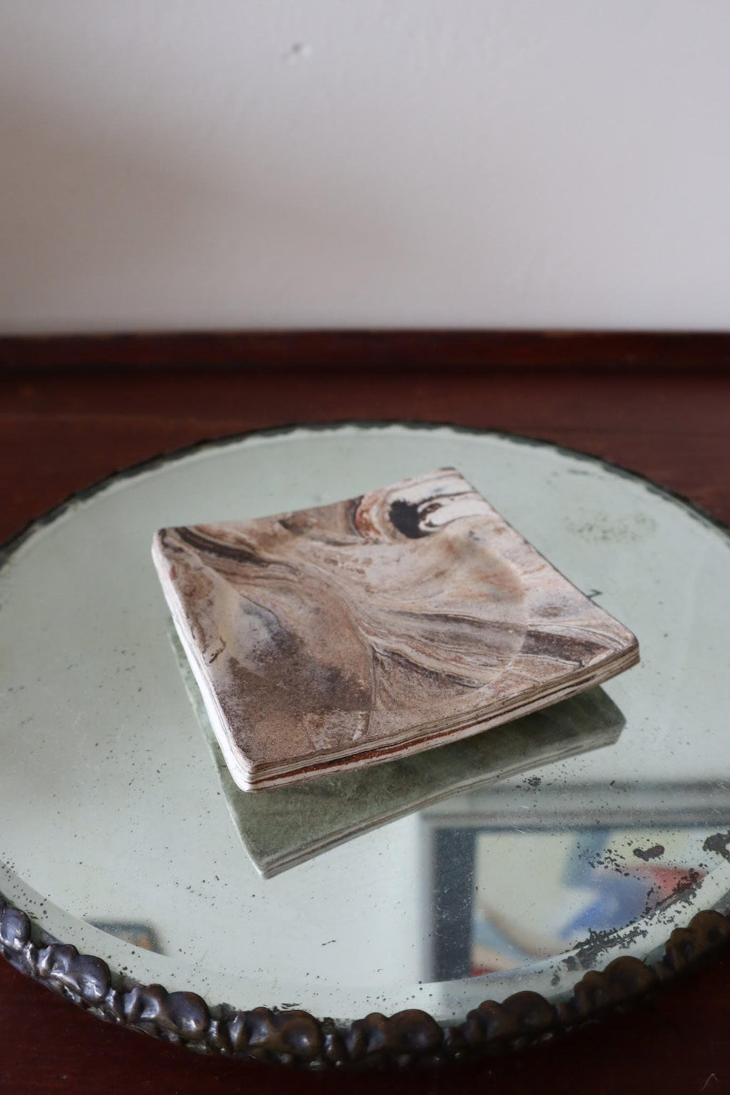 Marble-patterned coaster on a round mirror with a blurred background