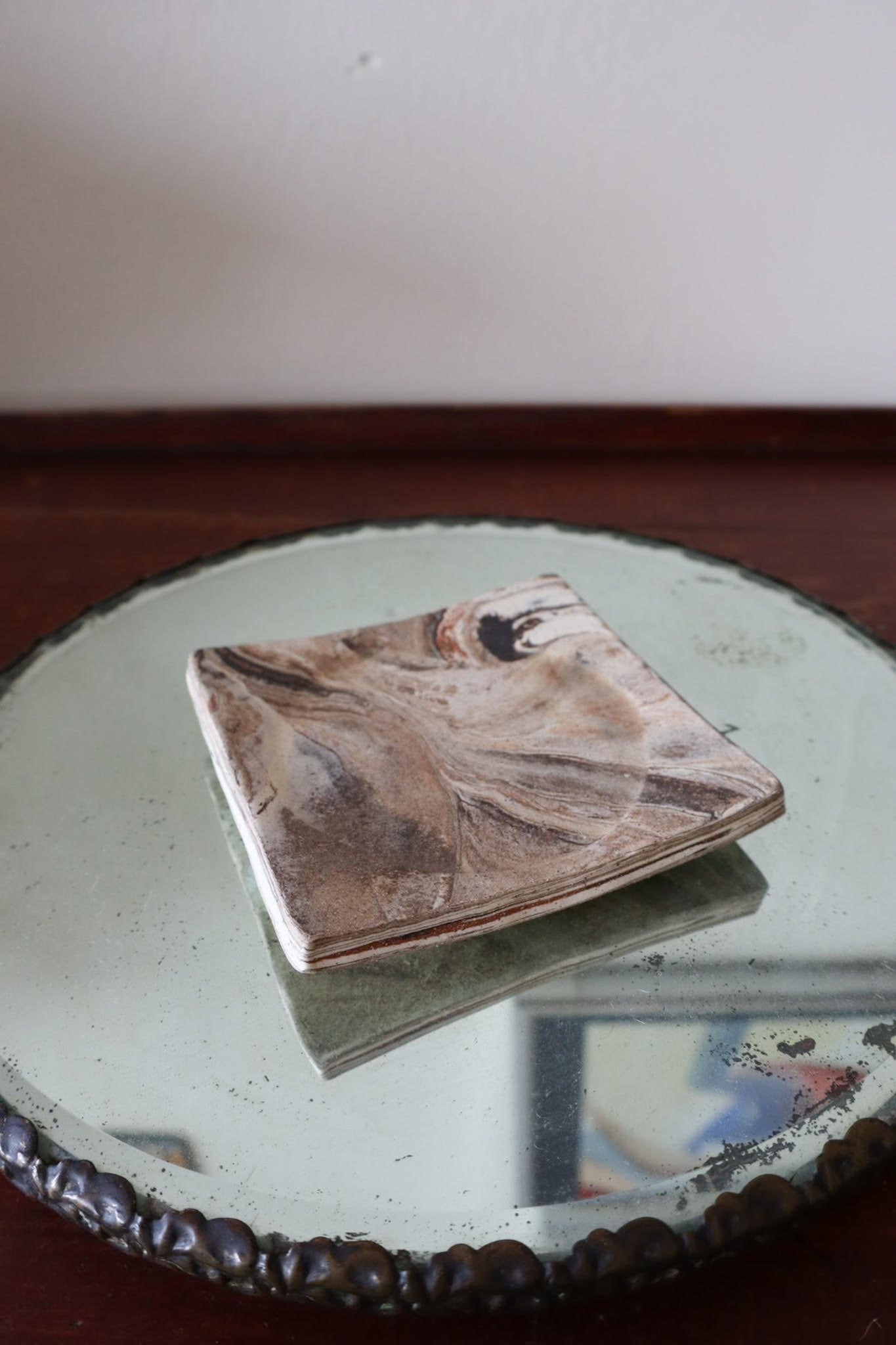 Marble-patterned coaster on a round mirror with a blurred background
