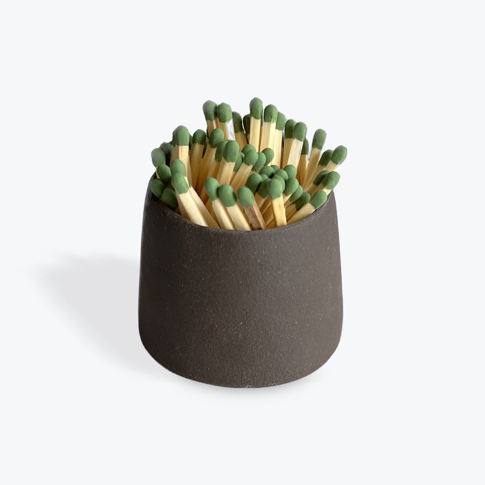 Matches with green tips in a dark ceramic match striker on a white background