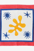 Napkin with a yellow motif and blue star patterns on a white background, bordered by red fabric.