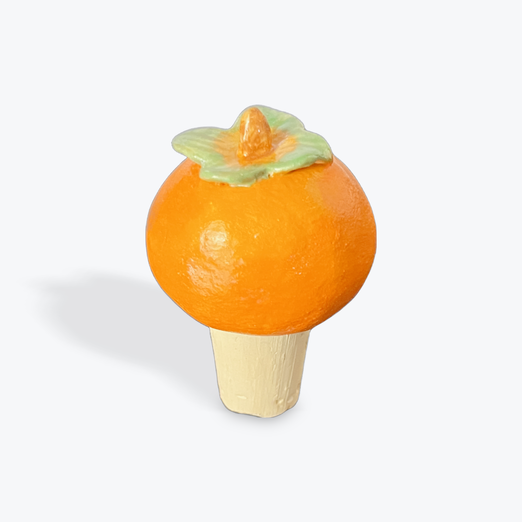 Persimmon-shaped bottle stopper with a green leaf on a white background