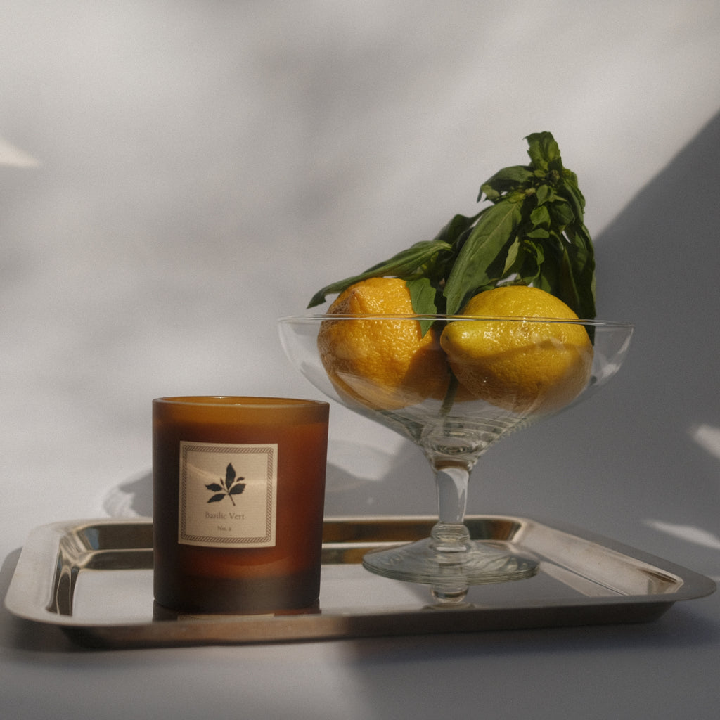 Candle and glass bowl with lemons on a tray against a neutral background