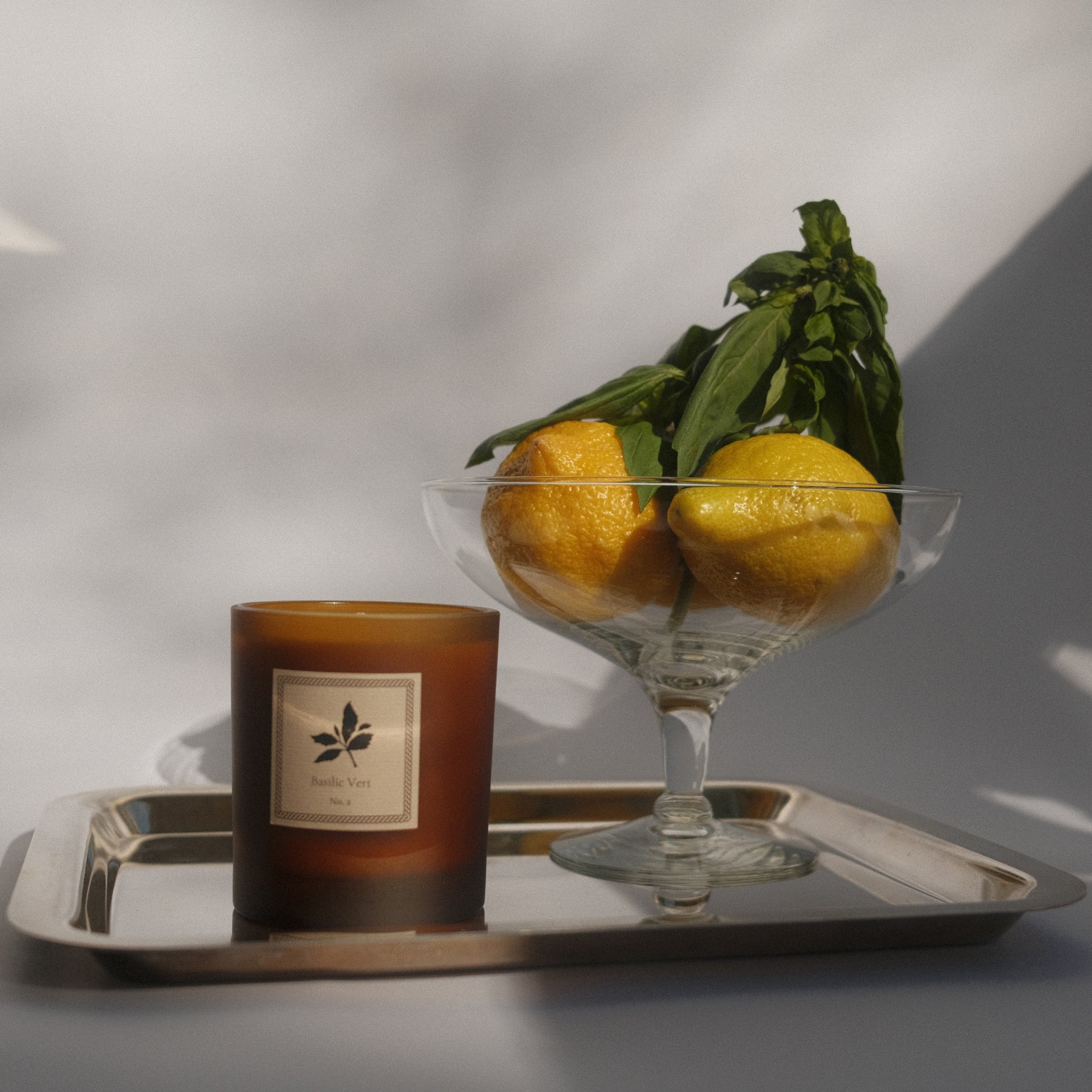 Candle and glass bowl with lemons on a tray against a neutral background