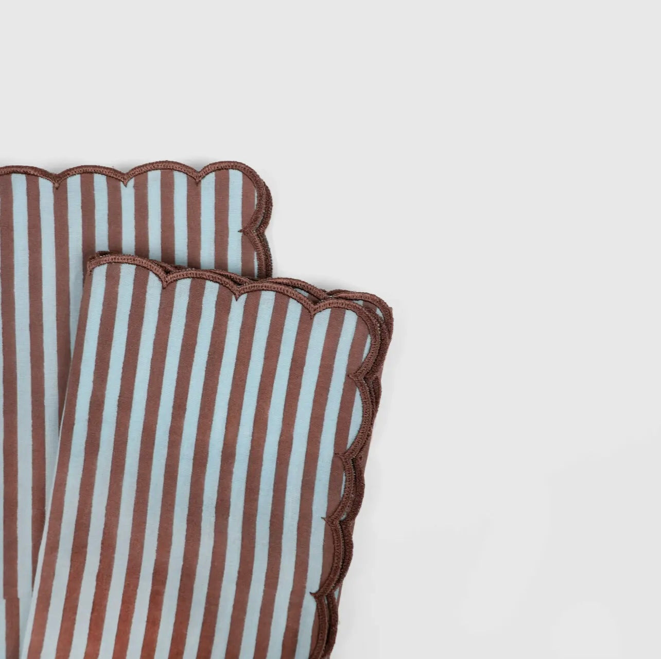 Pair of blue and brown stripe napkin with scalloped edge on a white background. 