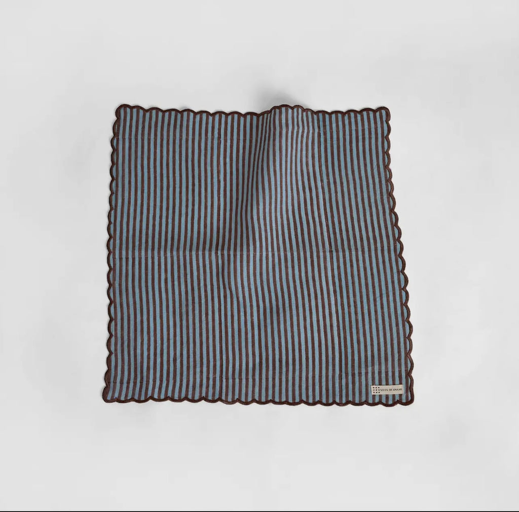 A blue and brown stripe napkin with scalloped edge on a white background. 