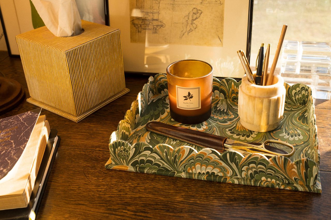 Candle on a decorative scalloped tray with stationery items on a wooden surface