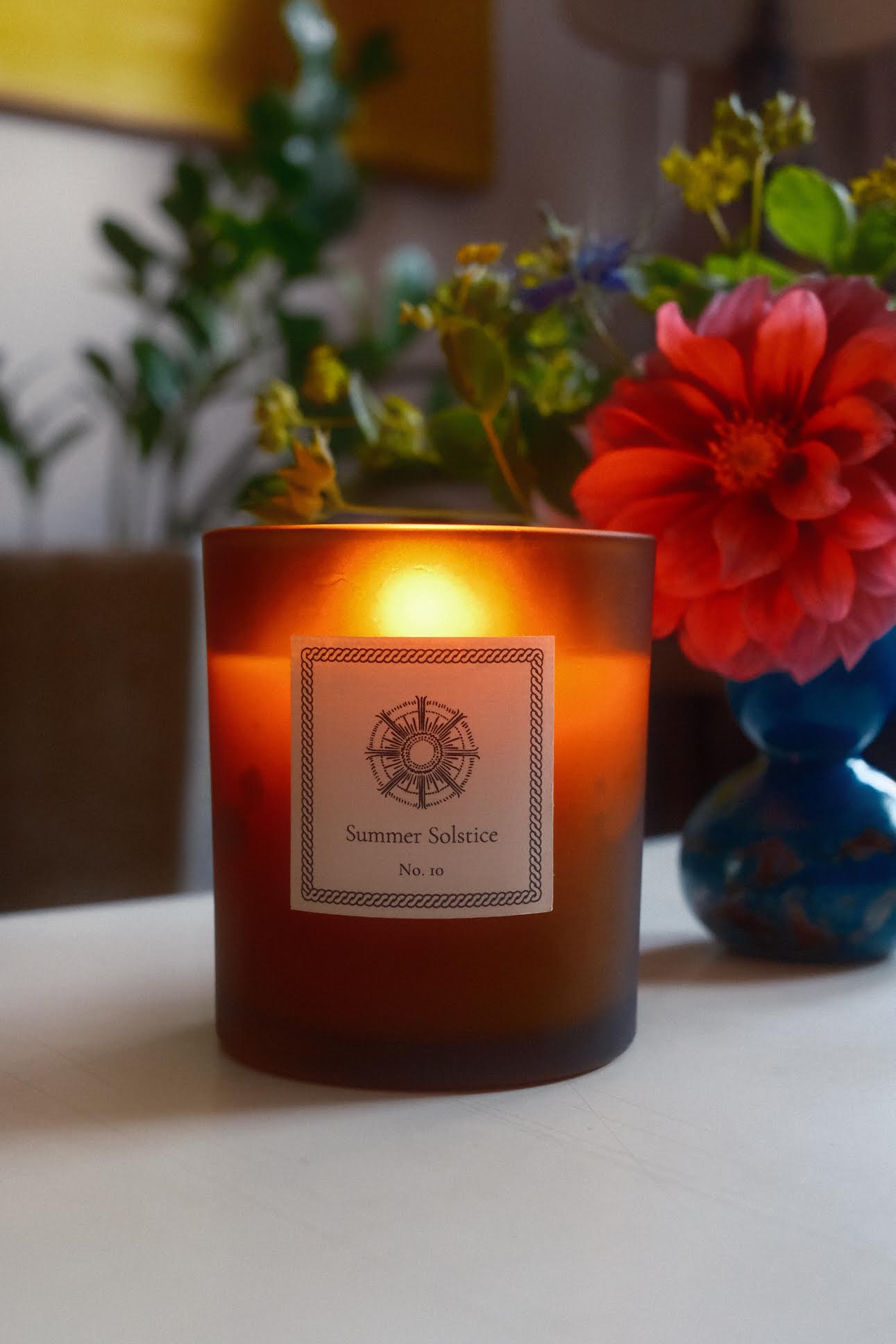 A glowing lit candle with a small bouquet of flowers sitting on a table. 