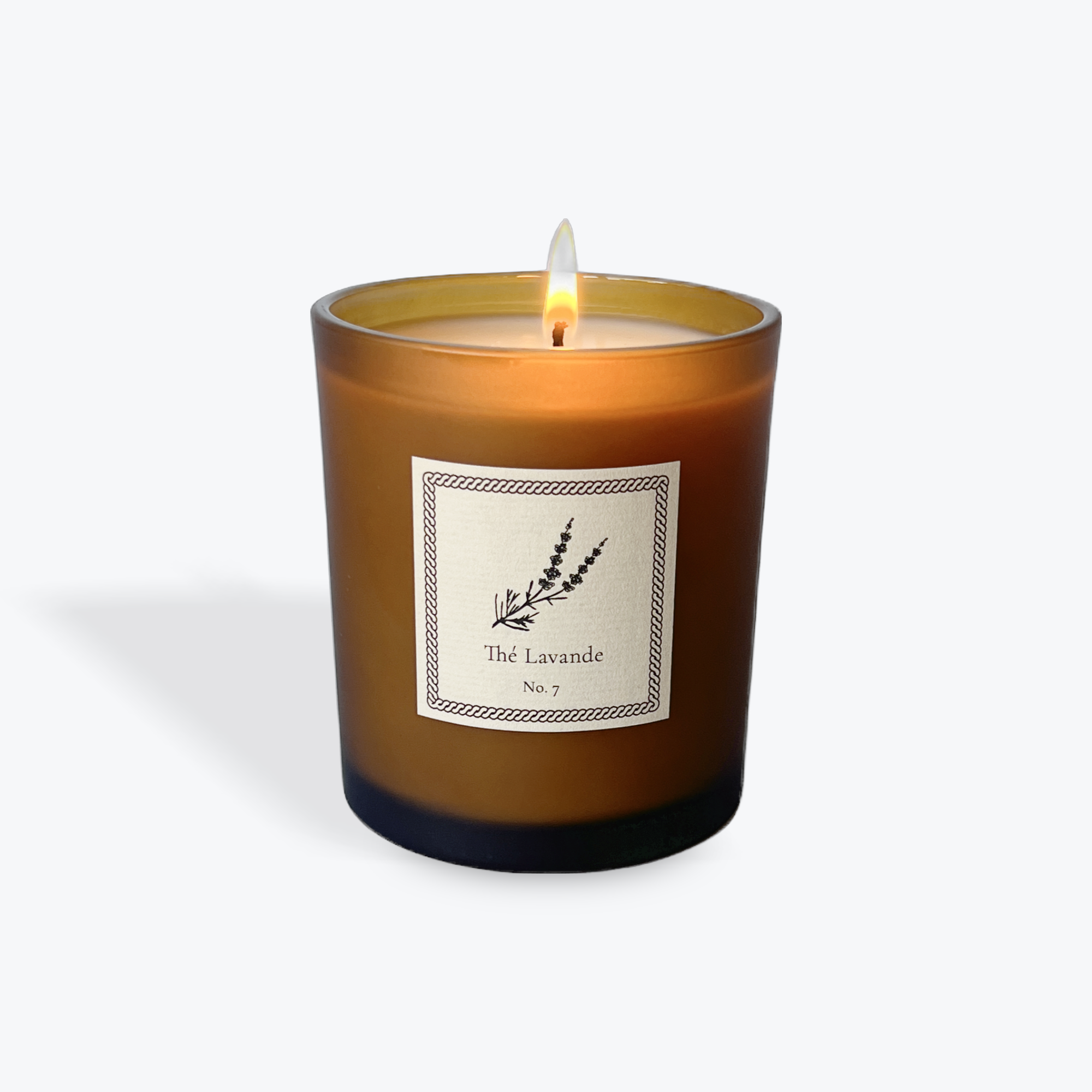 A lit amber glass scented candle with a white label reading 'The Lavande No. 7' and a lavender illustration, shown on a light gray background.