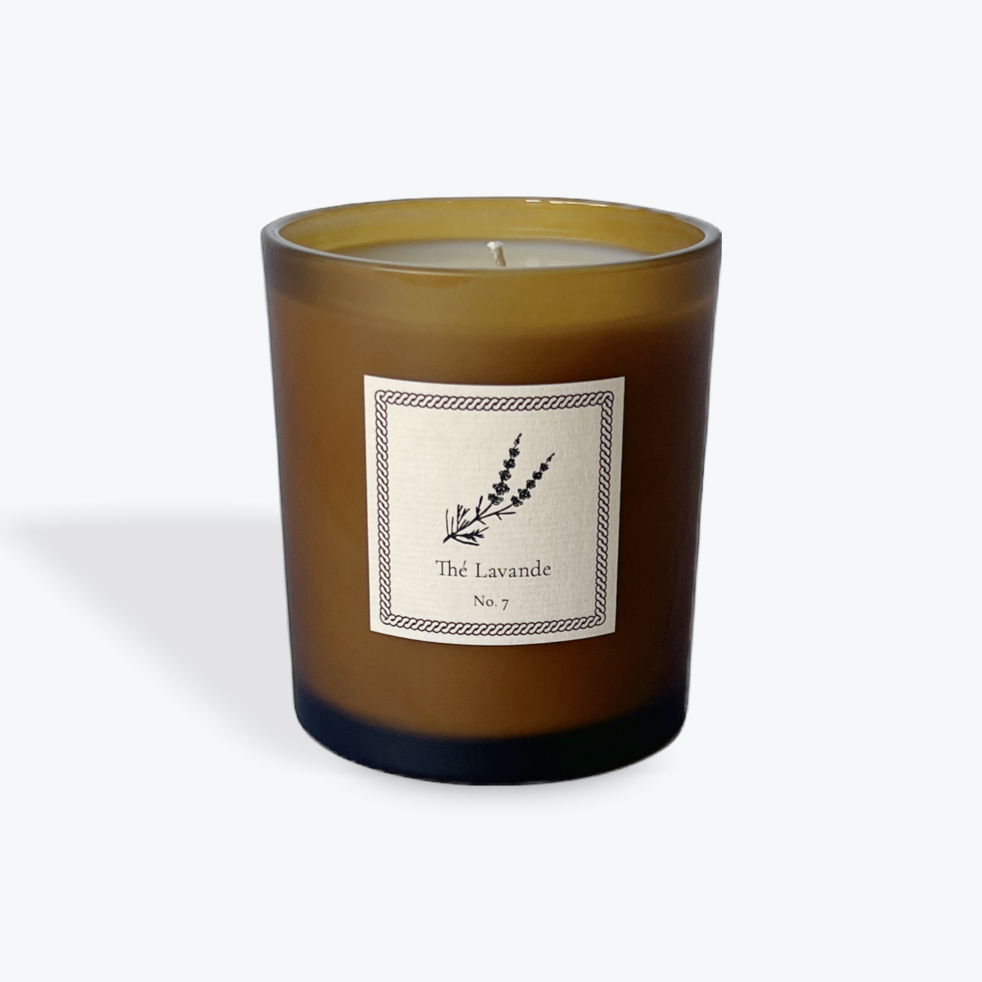 An amber glass jar candle with a white label reading 'The Lavande No. 7' and a botanical illustration, set against a light gray background.
