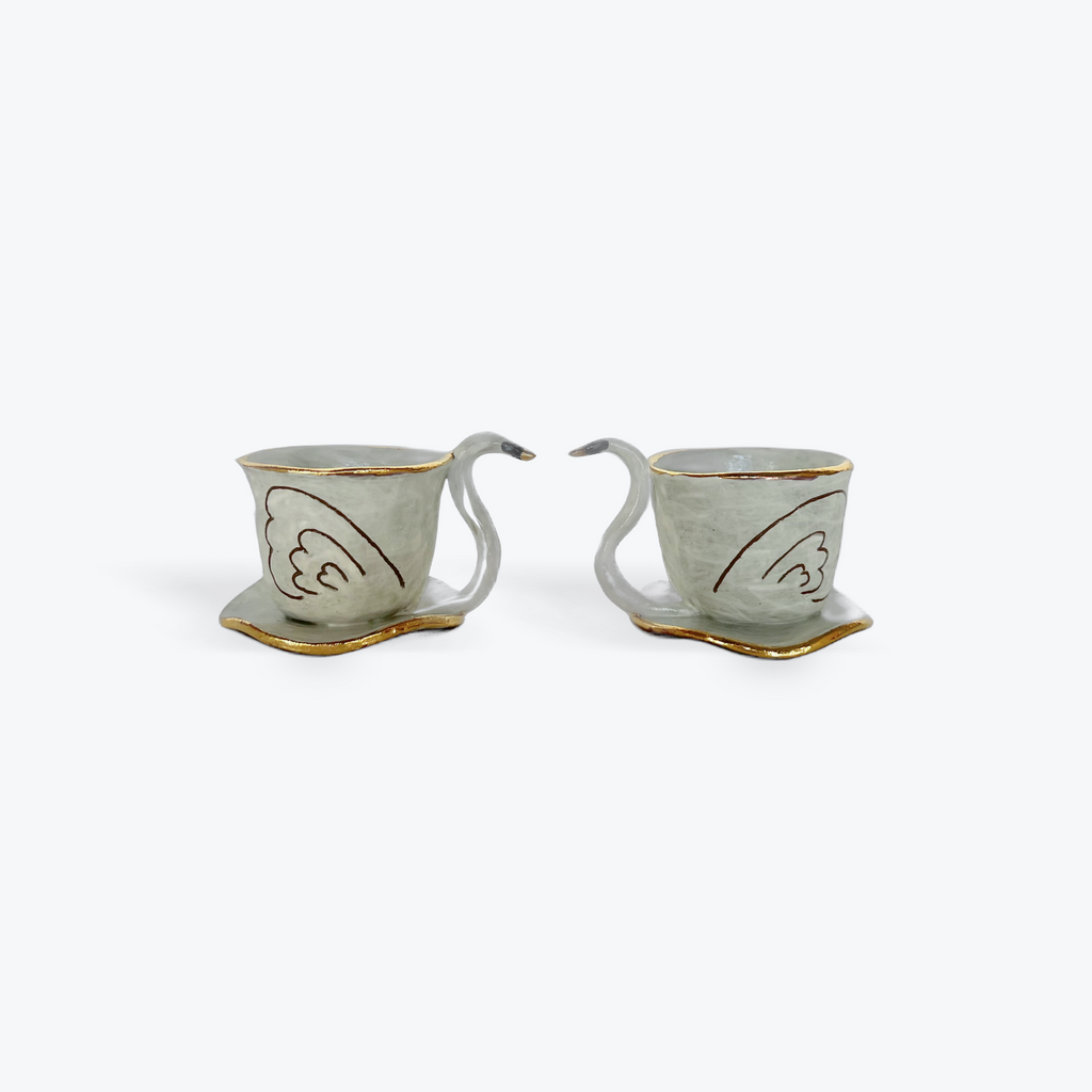 Two ceramic swan teacups with saucers on a white background